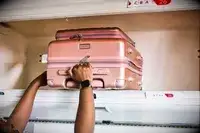A person putting the Calpak Ambeur Front Pocket Carry-on Luggage in an overhead compartment 