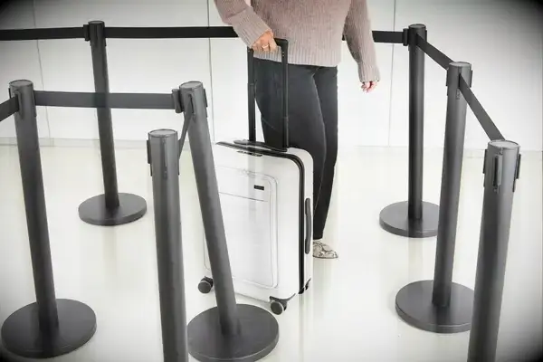 A person rolls the Away The Front Pocket Bigger Carry-On through an airport line