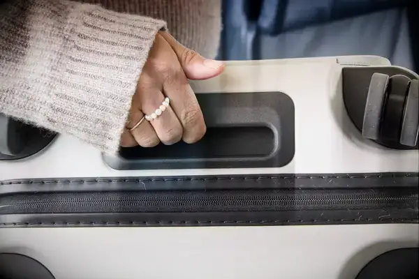A person carries the Away The Front Pocket Bigger Carry-On by the top handle
