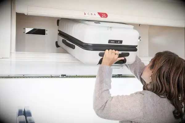 A person places the Away The Front Pocket Bigger Carry-On in an overhead compartment