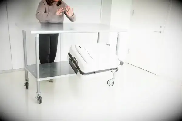 A person throws the Away The Front Pocket Bigger Carry-On off of a rolling cart