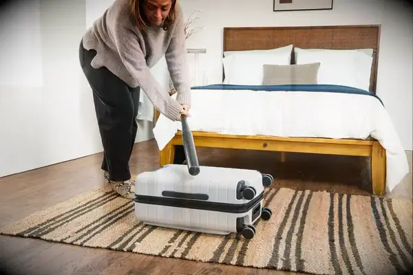 A person hits the Away The Front Pocket Bigger Carry-On with a baseball bat