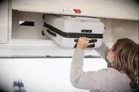 A person places the Away The Front Pocket Bigger Carry-On in an overhead compartment