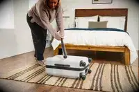 A person hits the Away The Front Pocket Bigger Carry-On with a baseball bat