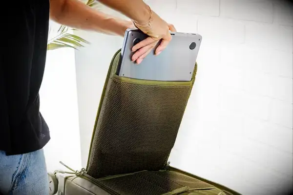 A person placing a laptop inside of a compartment in the Dagne Doverr Seattle Carry On Rolling Luggage 20.5