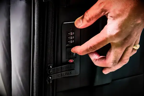 A hand touching the lock on the Calpak Luka Soft-Sided Carry-On Luggage