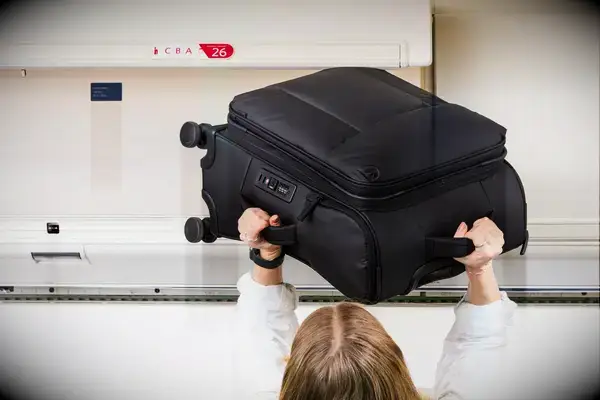 A person placing the Calpak Luka Soft-Sided Carry-On Luggage in an airplane overhead bin