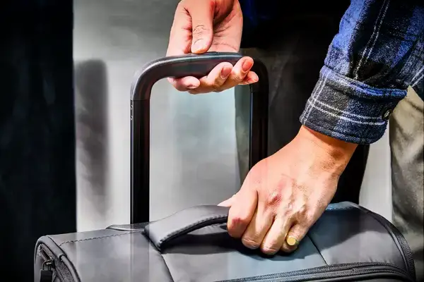 A person lifting the handle on the Calpak Luka Soft-Sided Carry-On Luggage