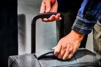 A person lifting the handle on the Calpak Luka Soft-Sided Carry-On Luggage