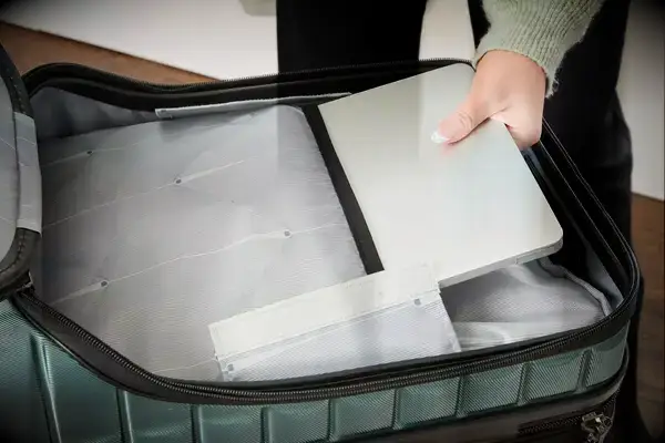 A person places a laptop into a pocket in the Delsey Paris Shadow 5.0 Carry-on with Laptop Compartment