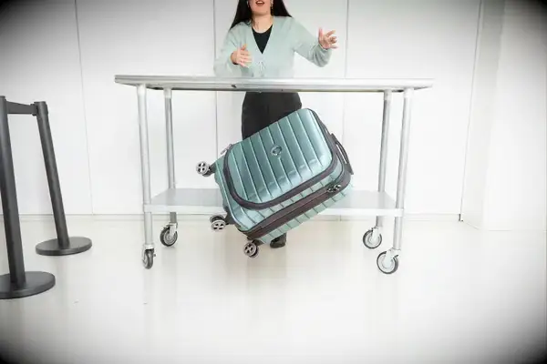 A person throws the Delsey Paris Shadow 5.0 Carry-on with Laptop Compartment off of a wheeled cart