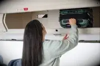 A person places the Delsey Paris Shadow 5.0 Carry-on with Laptop Compartment into an overhead compartment