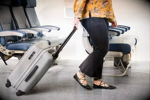 A person rolls the Monos Expandable Carry-on Pro over carpet