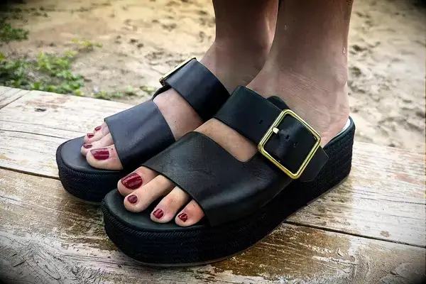 Close up view of a person wearing the Franco Sarto Taziana Espadrille Slide Sandals on a wood background