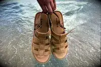 A person holding Bear Paw High Seas Iced Coffee Sandals in front of water