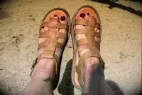 Front view of a person wearing the Bear Paw High Seas Iced Coffee Sandals with a background of sand