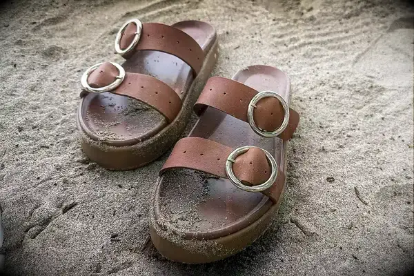 Beek Warbler Leather Platform Platform Leather Slides covered in sand with a sand background