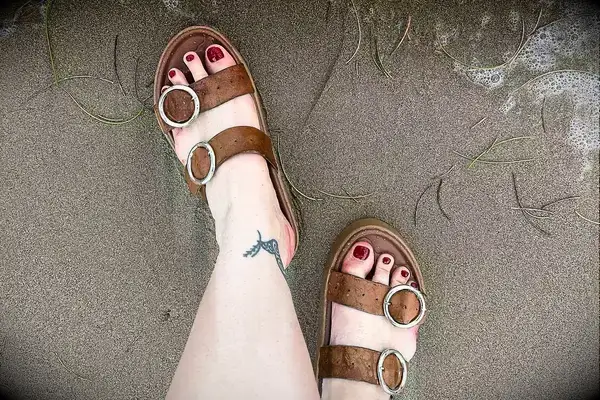 A person wearing the Beek Warbler Leather Platform Platform Leather Slides in the sand