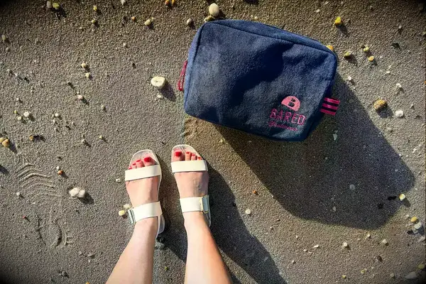 Top view of a person wearing the Bared Footwear Sanderlings on the sand with a bag