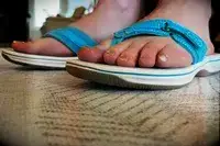 A closeup of feet wearing Clarks Womens Breeze Sea Flip Flops on rug