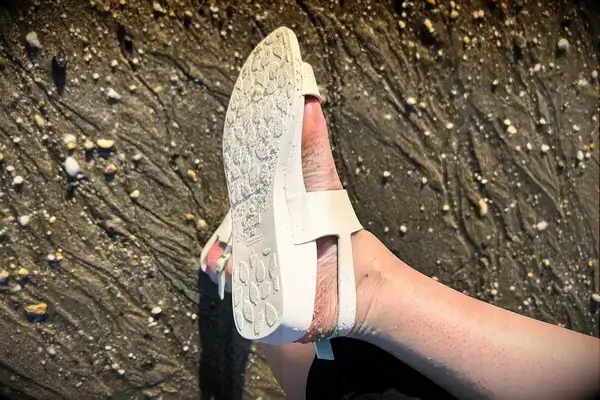 A person wearing the Bared Footwear Sanderlings showing the bottom of the shoe in the sand
