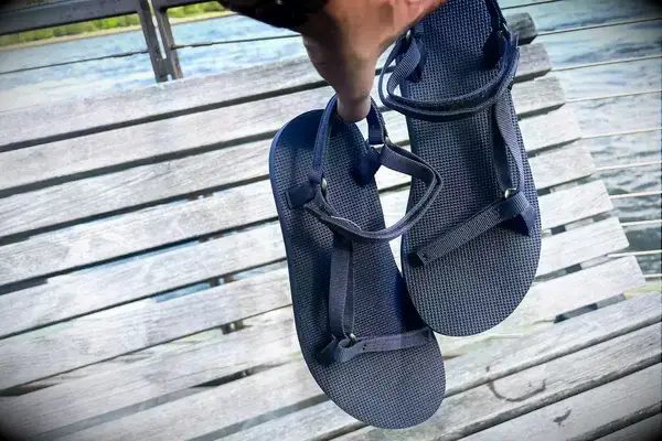 A person holding the Teva Original Universal Slim Sandal against a wood background