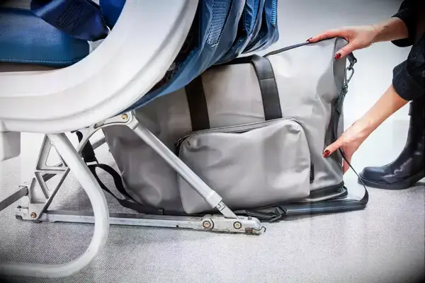 A person placing the July Carry All Weekender under an airplane seat