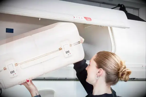 Person placing July Carry On Trunk in the overhead bin of an airplane