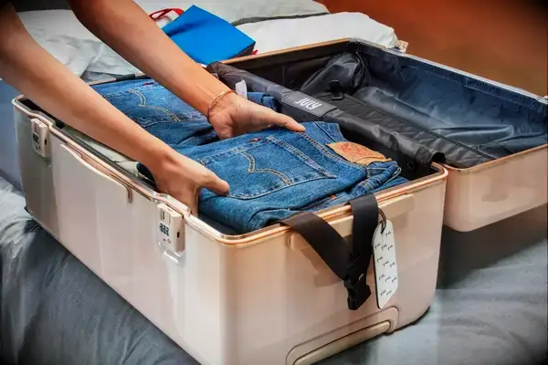 Hands packing jeans into a case from the July Trunk Set