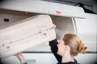 Person placing July Carry On Trunk in the overhead bin of an airplane