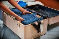 Hands packing jeans into a case from the July Trunk Set