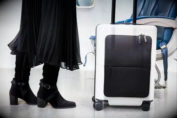 July Carry On Pro being rolled by a passenger in front of a row of seats on an airplane