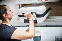 Person putting July Carry On Pro SnapSleeve into the overhead compartment of an airplane