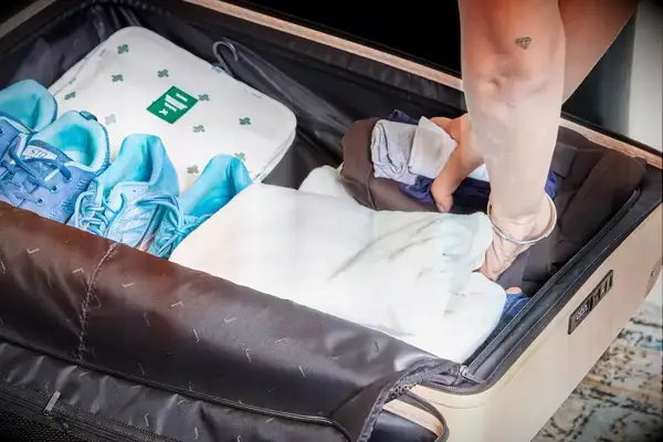 Hands placing clothing in the July Checked Plus Large Luggage