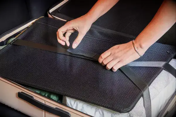 Hands strapping down clothing in the July Checked Plus Large Luggage