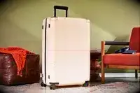 July Checked Plus Large Luggage displayed between a leather floor cushion and a chair