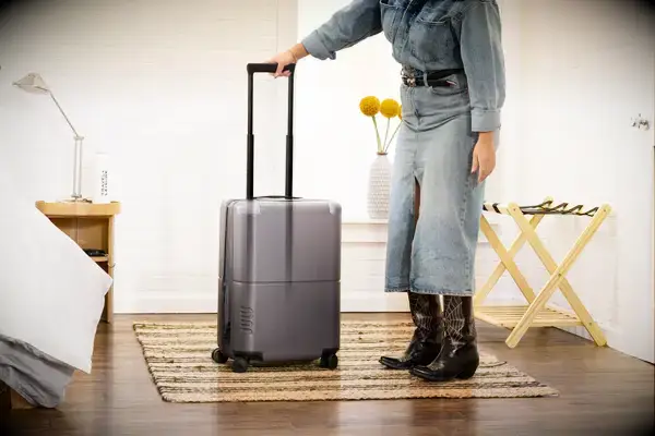 A person rolls the July Carry-on Max over a rug