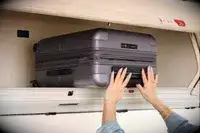 A person places the July Carry-on Max into an overhead compartment