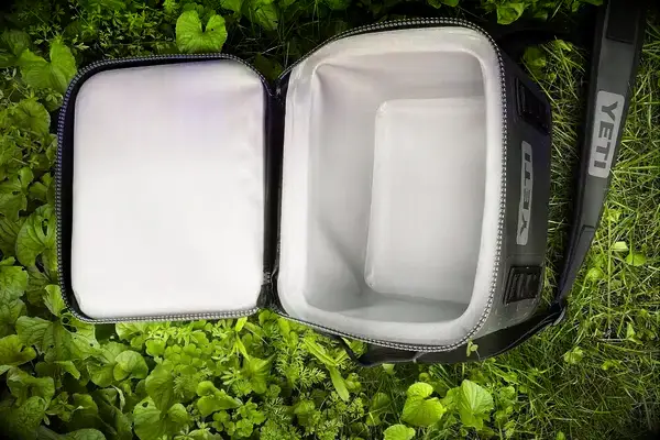 A Yeti Hopper Flip 12 Soft Cooler sits in foliage with its lid open