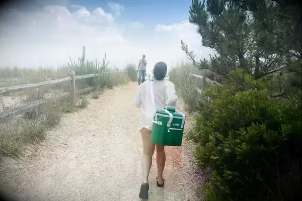 A person carries the RTIC Insulated Soft Cooler Bag on her shoulder while walking on a beach trail