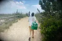A person carries the RTIC Insulated Soft Cooler Bag on her shoulder while walking on a beach trail