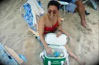 A person on a beach removes a canned beverage from the RTIC Insulated Soft Cooler Bag
