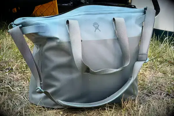 The Hydro Flask 26 L Day Escape Soft Cooler Tote sits in the grass