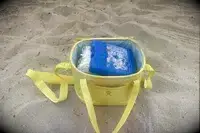 A Hydro Flask Carry Out Soft Cooler sits opened on the beach with an ice pack inside