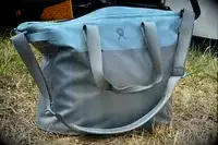 The Hydro Flask 26 L Day Escape Soft Cooler Tote sits in the grass
