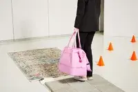Person carrying Béis The Weekender Travel Bag over a rug near cones