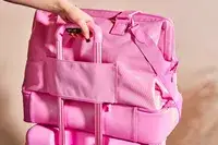 Hand on suitcase handle holding Béis The Weekender Travel Bag