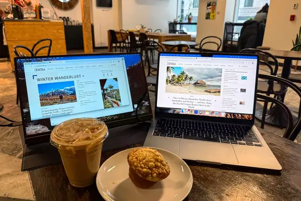 Opened ARZOPA Portable Monitor next to an opened macbook pro with a coffee and muffin in front.