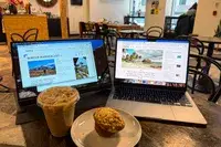 Opened ARZOPA Portable Monitor next to an opened macbook pro with a coffee and muffin in front.