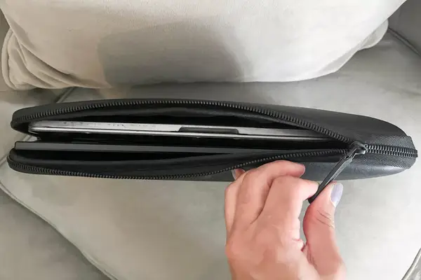 A hand zipping a laptop case containing the SideTrak Solo Pro Touch FHD 13.3